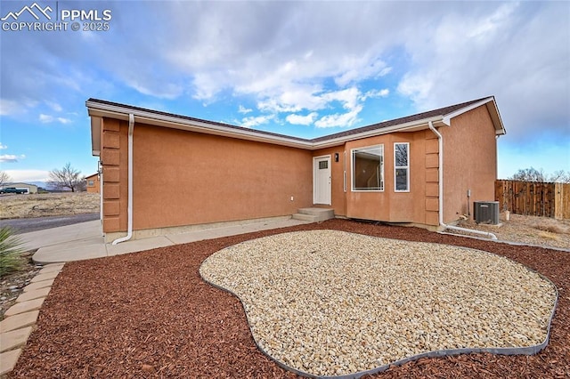 view of front facade with entry steps, central air condition unit, fence, and stucco siding