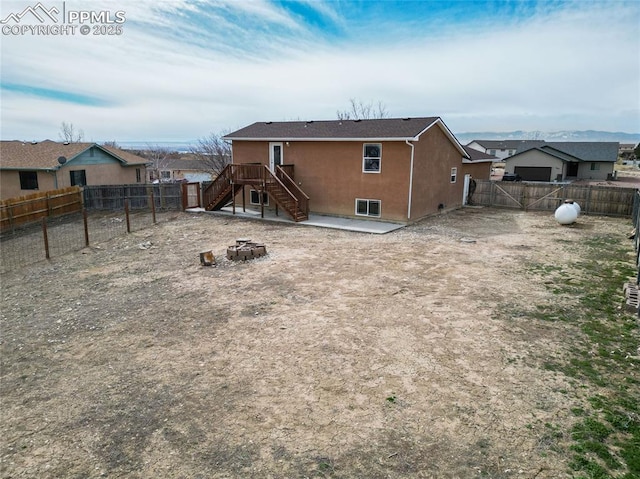 back of house with stucco siding, a fenced backyard, a fire pit, and stairs