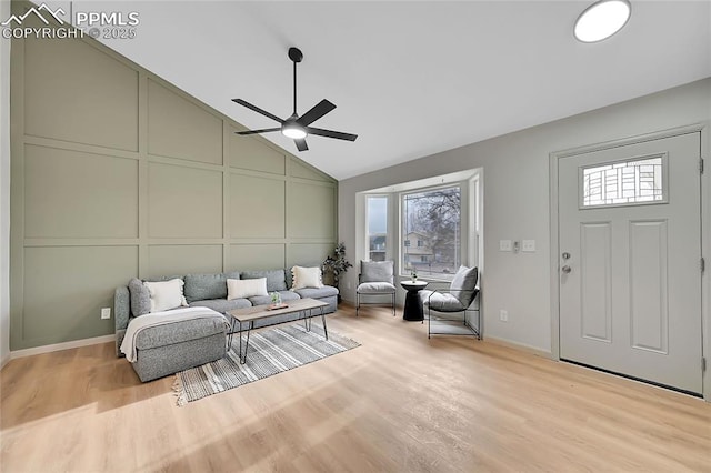 living room featuring lofted ceiling, ceiling fan, light wood-style flooring, and a decorative wall