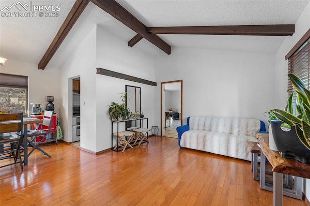 living area featuring vaulted ceiling with beams, a textured ceiling, and light wood-type flooring