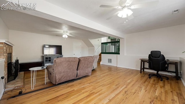 living area with ceiling fan, light wood-type flooring, a fireplace, and visible vents