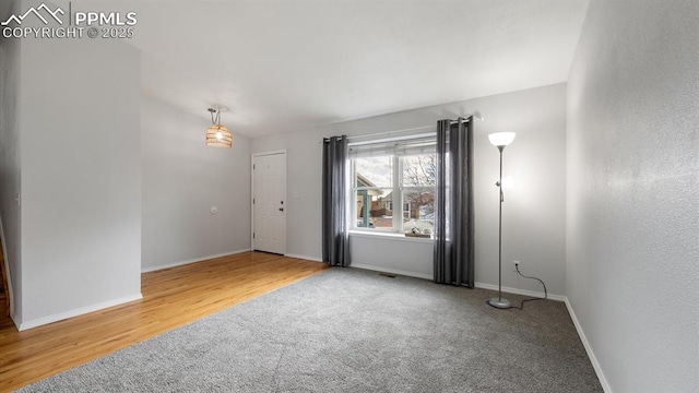 carpeted spare room featuring vaulted ceiling, baseboards, and wood finished floors