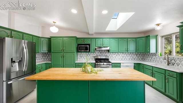 kitchen with vaulted ceiling with skylight, tasteful backsplash, stainless steel appliances, under cabinet range hood, and wooden counters