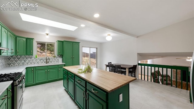 kitchen featuring a skylight, a sink, stainless steel gas range, a center island, and green cabinetry