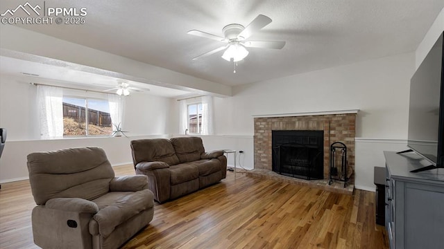 living room with ceiling fan, a textured ceiling, a fireplace, baseboards, and light wood-style floors