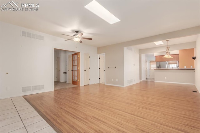 unfurnished living room with light wood finished floors, ceiling fan, a skylight, and visible vents