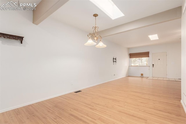 spare room with a chandelier, light wood-style flooring, a skylight, baseboards, and beamed ceiling