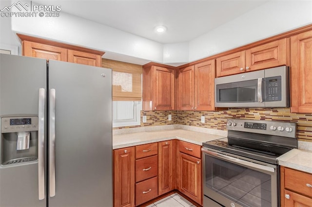 kitchen with tasteful backsplash, light countertops, appliances with stainless steel finishes, brown cabinetry, and light tile patterned flooring