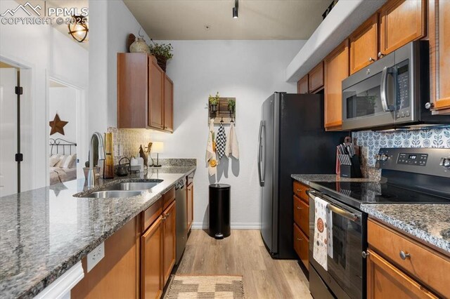 kitchen with tasteful backsplash, appliances with stainless steel finishes, brown cabinetry, a sink, and light wood-type flooring