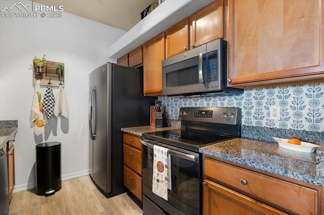 kitchen with decorative backsplash, dark stone counters, appliances with stainless steel finishes, brown cabinets, and light wood-type flooring