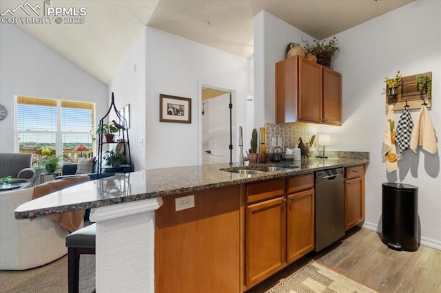 kitchen featuring a peninsula, a sink, stainless steel dishwasher, dark stone counters, and brown cabinetry