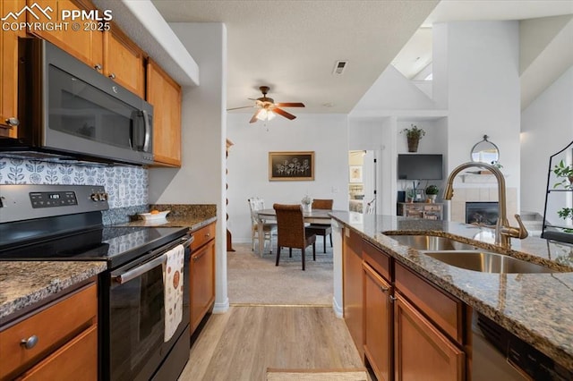 kitchen with electric range, dark stone counters, a tiled fireplace, brown cabinets, and a sink