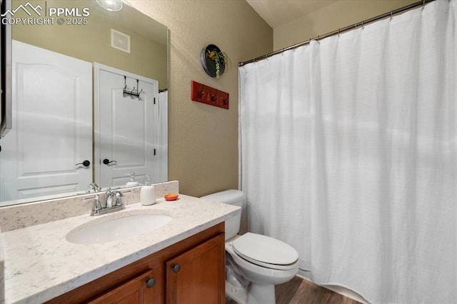 full bath featuring visible vents, a textured wall, toilet, vanity, and wood finished floors