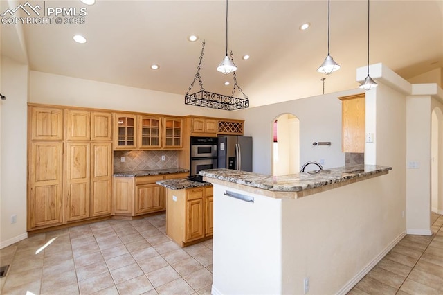 kitchen featuring dark stone countertops, arched walkways, appliances with stainless steel finishes, and a peninsula