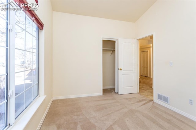 unfurnished bedroom featuring visible vents, multiple windows, light colored carpet, and baseboards