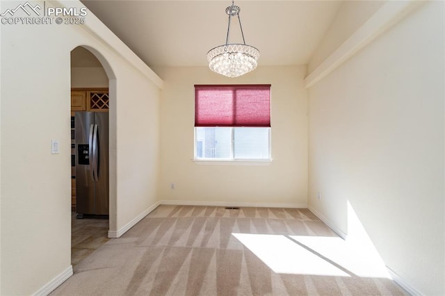 unfurnished room with baseboards, arched walkways, light colored carpet, and an inviting chandelier