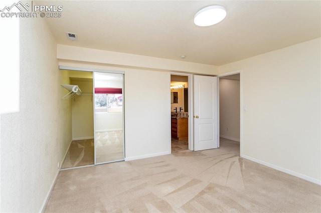 unfurnished bedroom with a closet, carpet flooring, ensuite bathroom, and baseboards