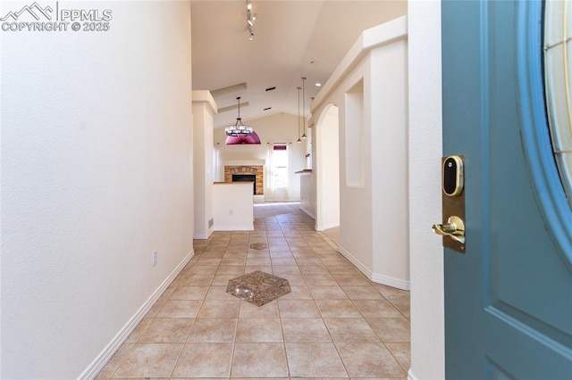 hall featuring lofted ceiling, track lighting, arched walkways, light tile patterned flooring, and baseboards