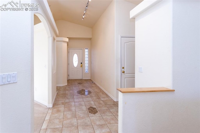 entryway featuring track lighting, baseboards, lofted ceiling, arched walkways, and light tile patterned flooring