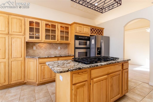 kitchen featuring arched walkways, stone counters, appliances with stainless steel finishes, and light tile patterned flooring