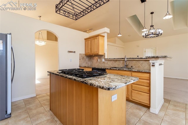 kitchen featuring light tile patterned floors, a kitchen island, arched walkways, freestanding refrigerator, and a sink