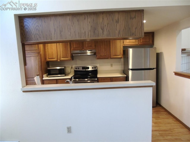 kitchen with under cabinet range hood, brown cabinets, appliances with stainless steel finishes, and light countertops