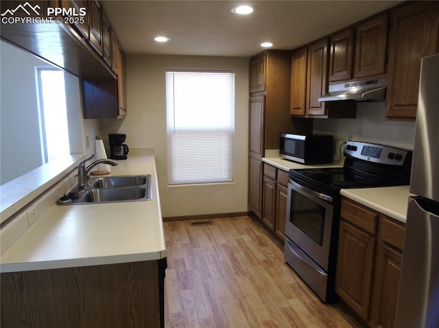 kitchen with light countertops, appliances with stainless steel finishes, under cabinet range hood, and a sink