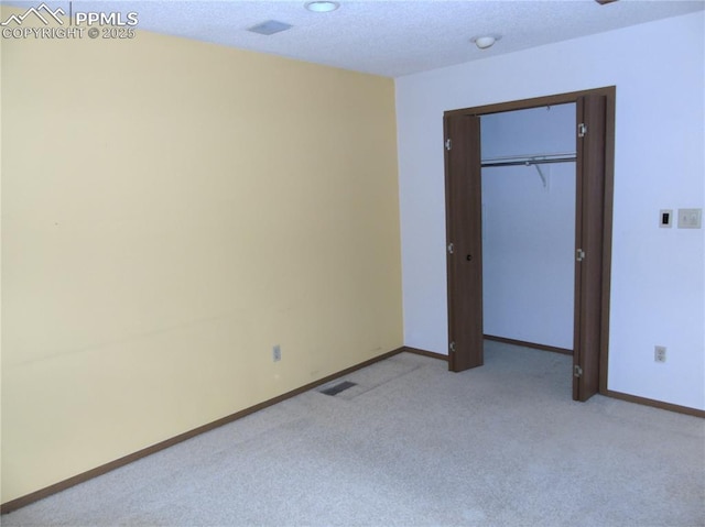 unfurnished bedroom featuring visible vents, baseboards, a closet, a textured ceiling, and light carpet