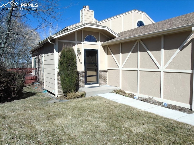 view of exterior entry with a yard, an attached garage, a shingled roof, brick siding, and a chimney