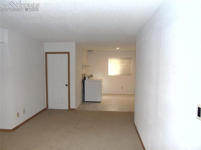 empty room featuring light carpet, washer / clothes dryer, baseboards, and a textured ceiling