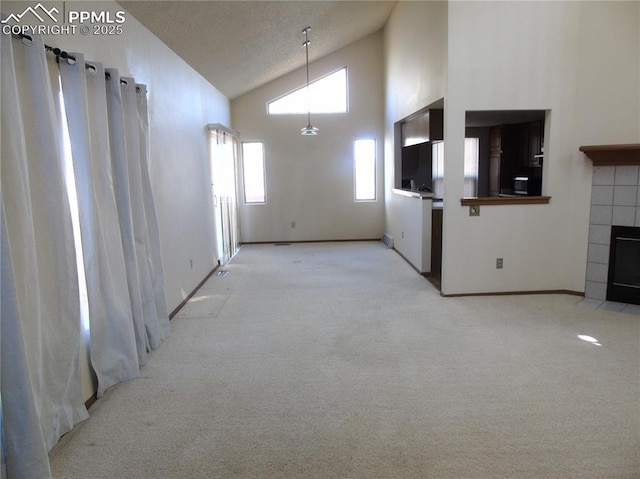 unfurnished living room with high vaulted ceiling, light colored carpet, and a tile fireplace