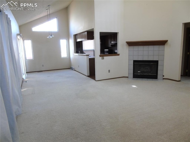 unfurnished living room featuring visible vents, high vaulted ceiling, carpet flooring, and a tile fireplace