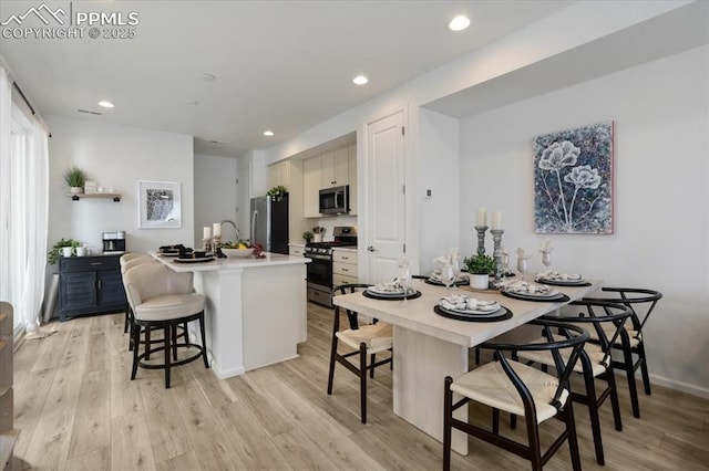 kitchen featuring light wood-type flooring, appliances with stainless steel finishes, light countertops, and a breakfast bar area