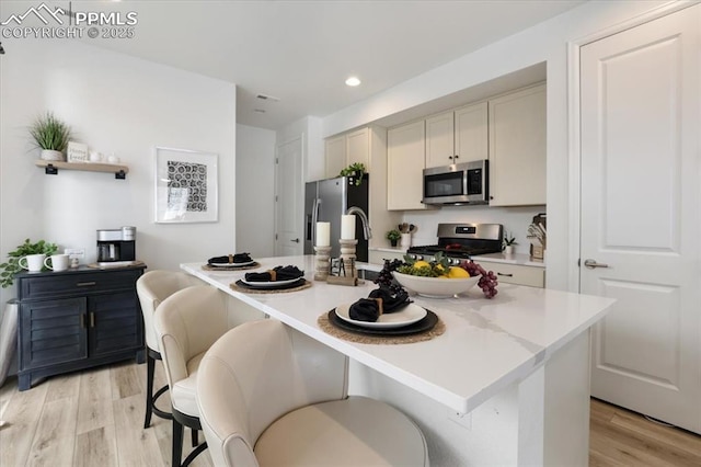 kitchen featuring a kitchen island with sink, stainless steel appliances, light countertops, light wood-type flooring, and a kitchen bar