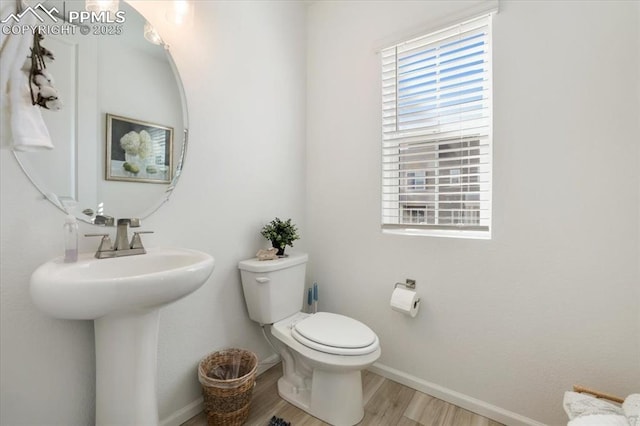 half bath featuring baseboards, a healthy amount of sunlight, toilet, and wood finished floors