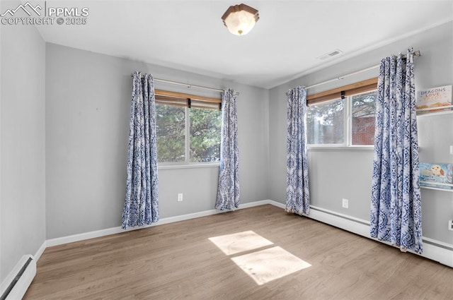 unfurnished room featuring visible vents, wood finished floors, baseboards, and a baseboard radiator