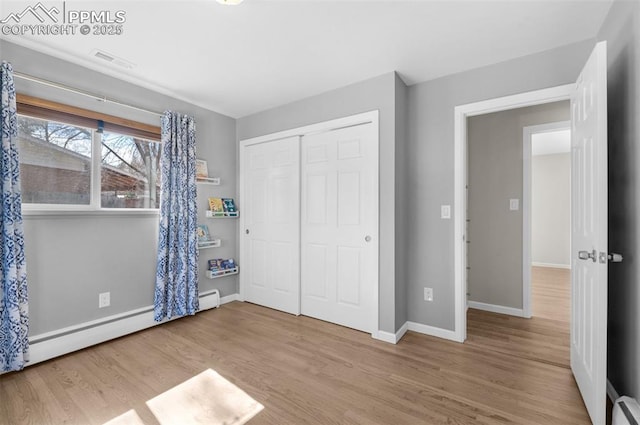 unfurnished bedroom with visible vents, baseboards, baseboard heating, wood finished floors, and a closet