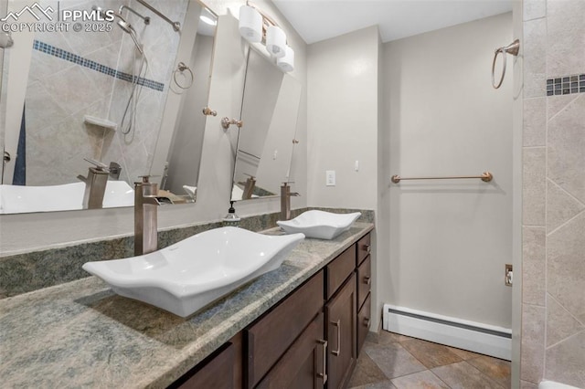 full bath featuring a tile shower, baseboard heating, double vanity, and a sink