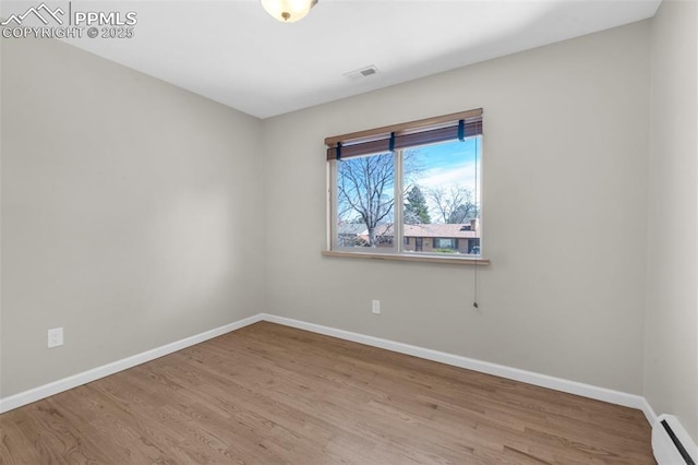 unfurnished room with visible vents, a baseboard heating unit, baseboards, and wood finished floors