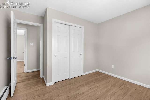 unfurnished bedroom featuring a closet, baseboards, light wood finished floors, and a baseboard radiator