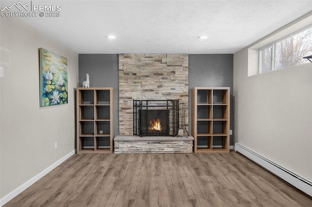 unfurnished living room featuring wood finished floors, baseboards, recessed lighting, a stone fireplace, and a baseboard heating unit