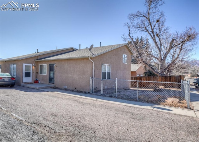 back of property featuring a shingled roof, a fenced front yard, crawl space, a gate, and stucco siding