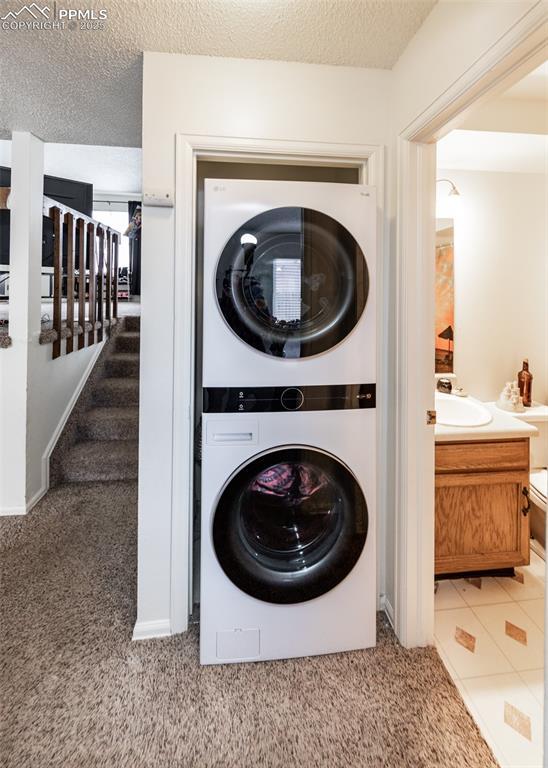997 Magnolia St, Colorado Springs, CO 80907 - laundry room with a sink, a textured ceiling, stacked washing maching and dryer, carpet, and laundry area