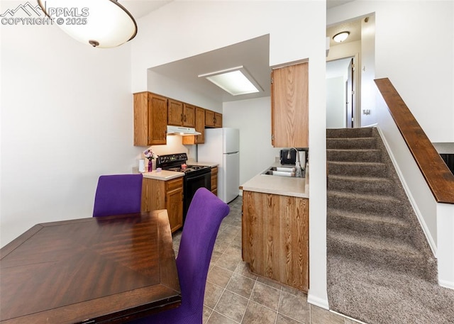 kitchen featuring under cabinet range hood, a sink, freestanding refrigerator, brown cabinets, and black electric range oven