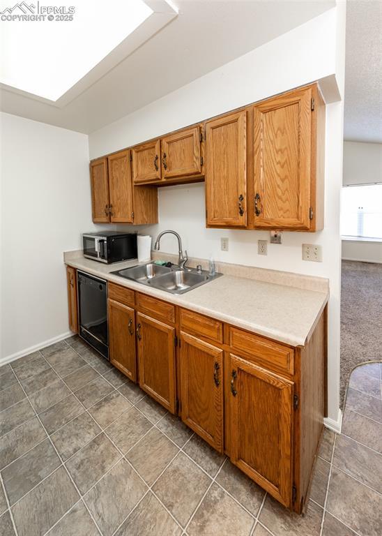 kitchen with a skylight, stainless steel microwave, brown cabinetry, a sink, and dishwasher