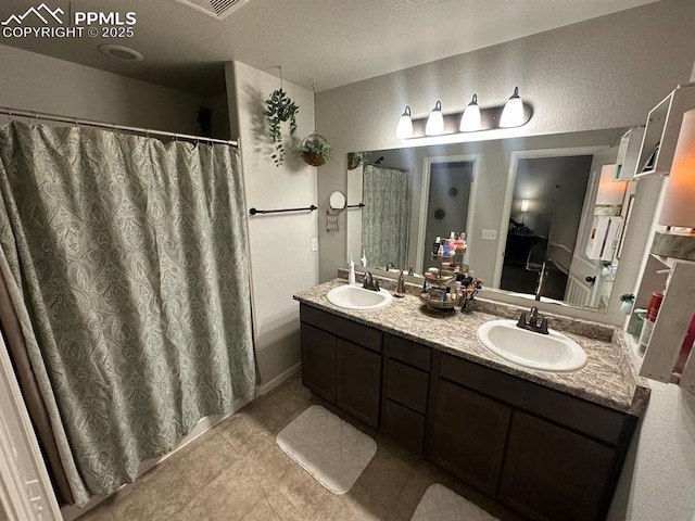 full bath featuring a textured ceiling, double vanity, a textured wall, and a sink