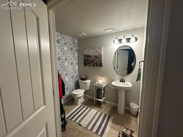 full bathroom with visible vents, baseboards, a textured ceiling, toilet, and a textured wall