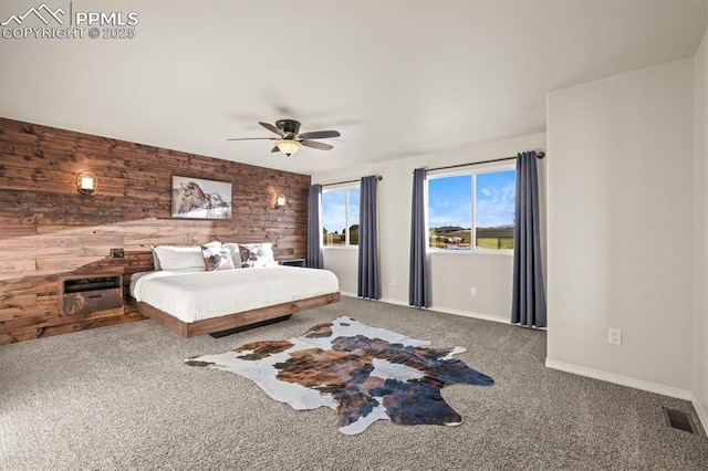 carpeted bedroom with baseboards, visible vents, ceiling fan, an accent wall, and wood walls