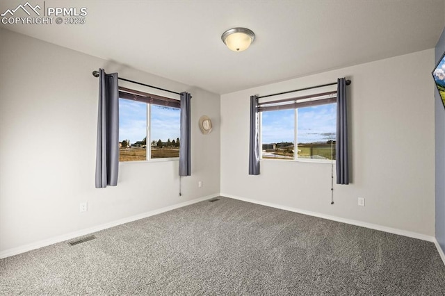 unfurnished room featuring visible vents, dark carpet, a wealth of natural light, and baseboards