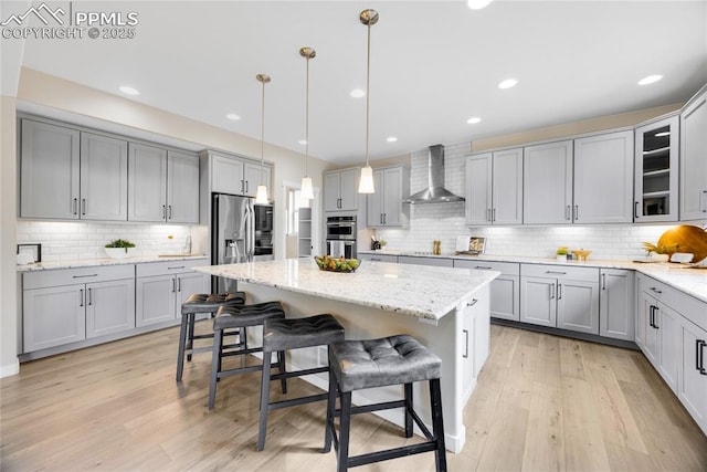 kitchen with light wood-style flooring, appliances with stainless steel finishes, a breakfast bar area, gray cabinets, and wall chimney range hood